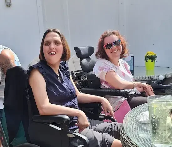 Complex care clients enjoying time in the garden Two smiling women in wheelchairs enjoying time outdoors in the sun