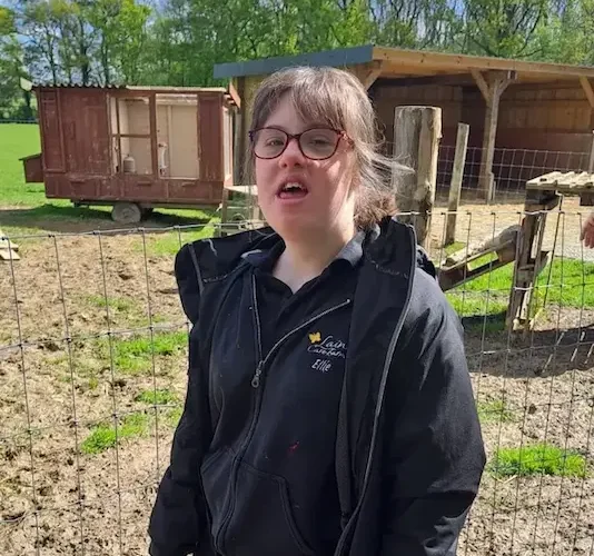 Client at Lainey’s Care Farm – Outdoor Activities Young woman in outdoor gear standing in front of a farm enclosure at Lainey’s Care Farm.
